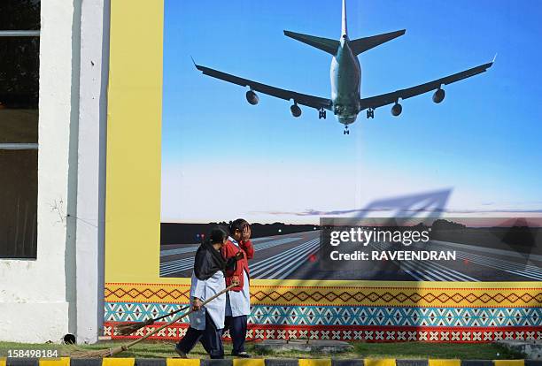 Indian sweepers walk past a billboard of an aircraft on final approach outside the venue of the 2nd India-ASEAN Business Fair and Business Conclave...