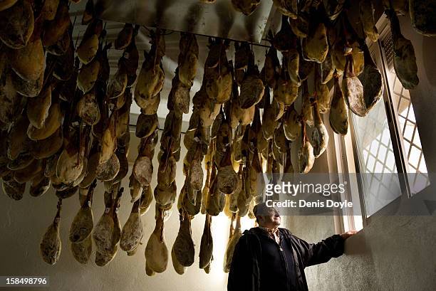 Faustino Prieto, owner of the small family-run Iberian ham business looks out the window beside legs of dry-cured Jamon Iberico de bellota in the...
