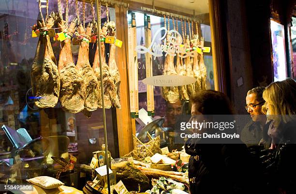 Pedestrians look at the window display of the Alberto Lopez Araque jamon Iberico shop on December 14, 2012 in Madrid, Spain. Dry-cured Iberian ham or...