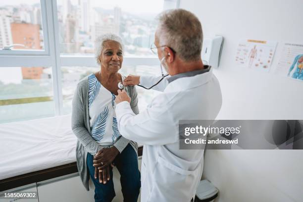 portrait of a doctor listening to an elderly woman patient's heartbeat - listening to heartbeat 個照片及圖片檔