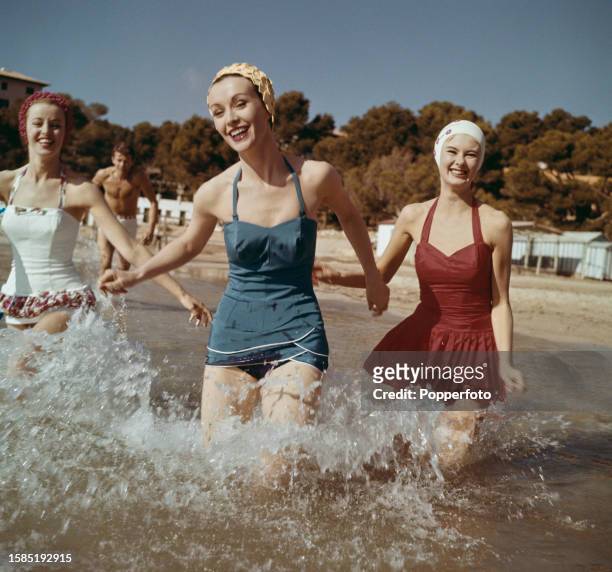 Posed vacation scene of three female fashion models wearing, from left, a white batiste swimsuit with a band of ruched printed cotton, a blue...