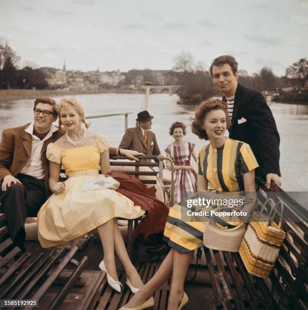 Group of men and women standing and seated on the top deck of a boat as it cruises down the River Thames, with Richmond Bridge visible in the...