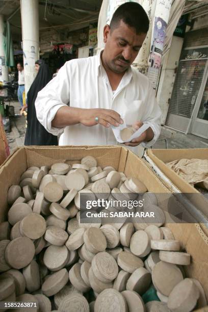 Vendor selects four clay tablets to packet together ready to sell at his stand outside the Imam Musa al-Kadim mosque in the Shiite Muslim...
