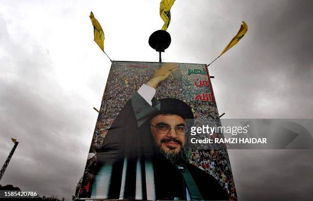Hezbollah flags flutter over a huge poster of Hezbollah chief Hassan Nasrallah reading in Arabic "Victory is from God" in the southern Lebanese...