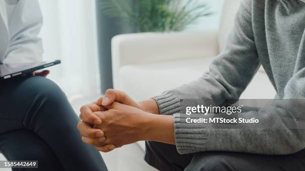 closeup of young asian female psychotherapist discussing a problem and touch hand young depressed sit on couch at clinic. medical insurance, mental health. - schizofrenie stockfoto's en -beelden