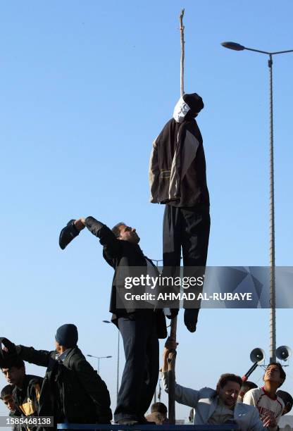 An Iraqi in the Shiite-majority Baghdad suburb Sadr City uses a shoe to beat an effigy of ousted dictator Saddam Hussein hanging from a rope as they...