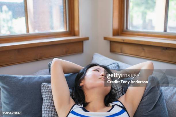 young woman lounging on sofa looking out window - korean ethnicity stock pictures, royalty-free photos & images