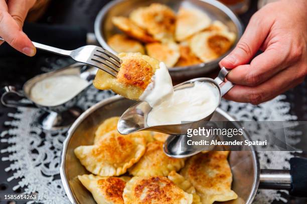 man dipping pierogi dumplings in sour cream, close-up - daily life in warsaw poland stock-fotos und bilder