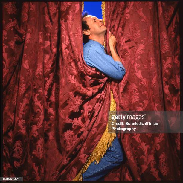 Comedian Billy Crystal poses clutching two red curtains in Los Angeles in 1986.