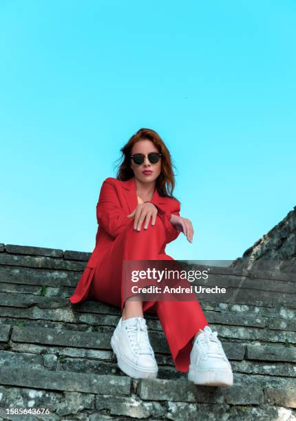 woman in red suit and white sneakers sitting on stairs, low angle view - running shoes sky ストックフォトと画像