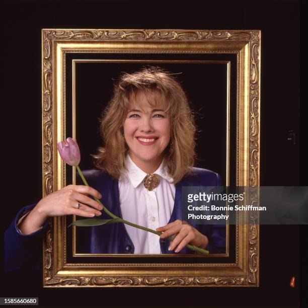 Actor Catherine O'Hara smiles from behind an ornate gold frame and holds a tulip in front of the frame in Los Angeles in 1986.