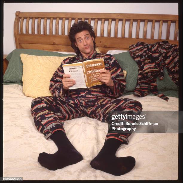 Comedian Richard Lewis leans back on a bed wearing matching pajamas and reads "Prisoners of Childhood" by Alice Miller in Los Angeles in 1989.
