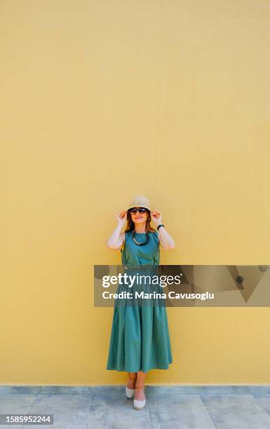 woman in a hat and sunglasses wearing green summer dress standing near the wall. - blue white summer hat background stock pictures, royalty-free photos & images