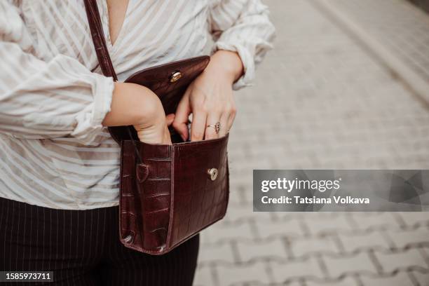 hands of unrecognizable female student rummaging in crossbody bag, looking for small thing throughout walking on street. - bolso cruzado fotografías e imágenes de stock