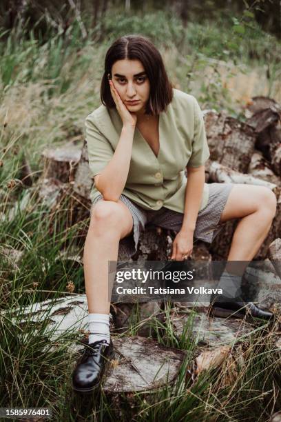 confident young lady relaxing on logs with speed legs wide, leaning head on hand and looking at camera with serious expression. - woman leg spread stock pictures, royalty-free photos & images