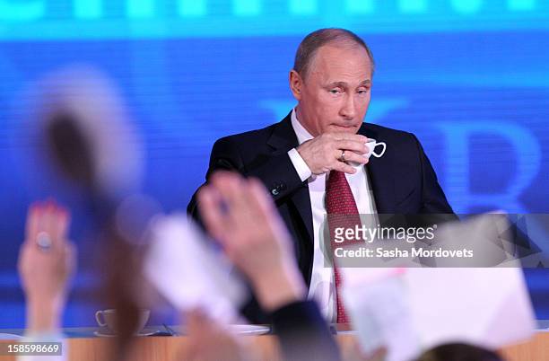 Russian President Vladimir Putin holds a cup as journalists raise their hands during his end of year press conference on December 20, 2012 in Moscow,...