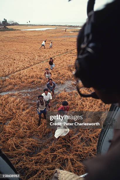 Helicopter crew member drops food to villagers in a remote region of Bangladesh as they reach up for the emergency supplies. As a result of one of...