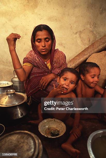 Widow sits with her children as they eat their dinner in their one-roomed house. This is the main and often only meal of the day for this...