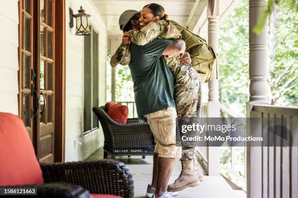 portrait of veteran husband embracing wife/female u.s. soldier wearing 2023 ocp uniform in front of suburban home - military uniform at home stock pictures, royalty-free photos & images