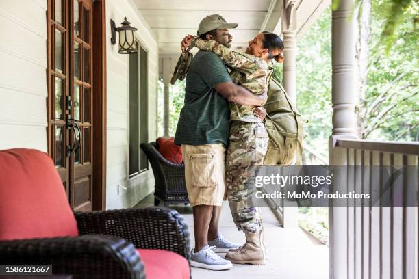 portrait of veteran husband embracing wife/female u.s. soldier wearing 2023 ocp uniform in front of suburban home - military uniform at home stock pictures, royalty-free photos & images