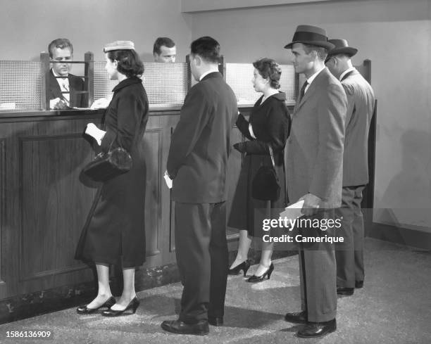 Line of people at the bank teller's window await their turn.