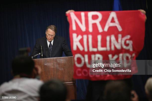 Demonstrator from CodePink holds up a banner as National Rifle Association Executive Vice President Wayne LaPierre delivers remarks during a news...