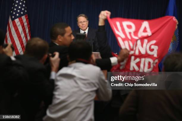 Demonstrator from CodePink holds up a banner as National Rifle Association Executive Vice President Wayne LaPierre delivers remarks during a news...