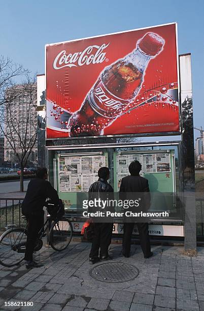 Passersby catch up on the latest news with newspapers posted on a notice board under a Coca-Cola sign on Jianguomenwai Avenue. Newspapers and...