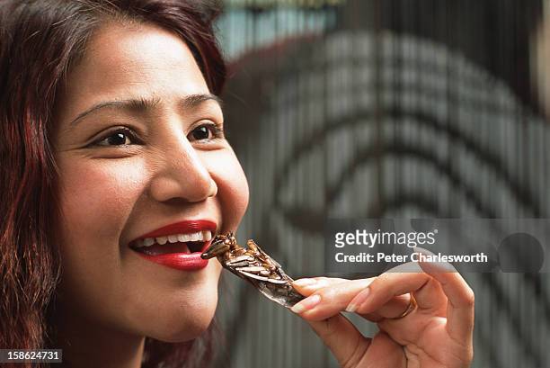 Anita Chaisatuen, owner of a hair salon, eats fried insects for a lunchtime snack. Cooked Insects are very popular in Thailand. She is seen eating a...