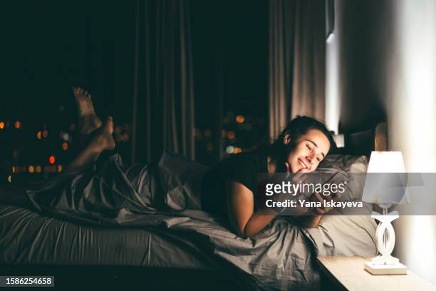late night shot of a happy person lying in bed using the phone to surf the social media before sleep. gadget addiction, bad habits leading to insomnia, and digital detox - relation à distance photos et images de collection