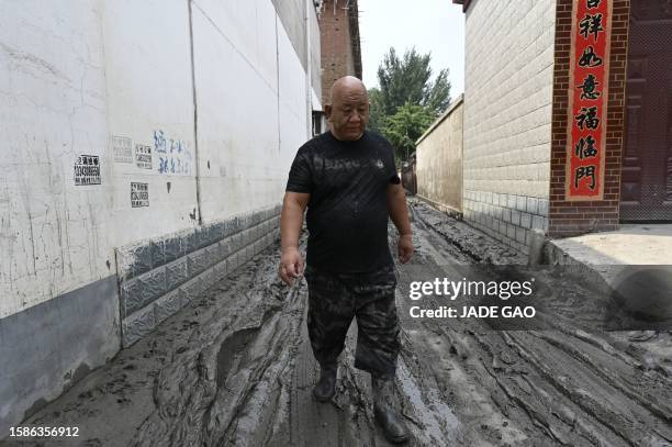 Local resident walks along a muddy street in the aftermath of flooding from heavy rains in Zhuozhou city, in northern China's Hebei province on...
