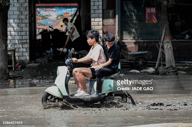 Local residents ride a scooter through a muddy street in the aftermath of flooding from heavy rains in Zhuozhou city, in northern China's Hebei...