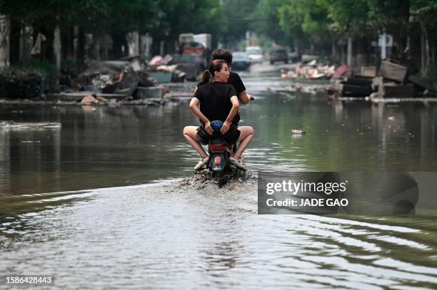 Local residents ride a scooter on a flooded street in the aftermath of flooding from heavy rains in Zhuozhou city, in northern China's Hebei province...
