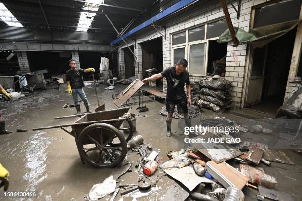 Workers clear mud and debris from a warehouse in the aftermath of flooding from heavy rains in Zhuozhou city, in northern China's Hebei province on...