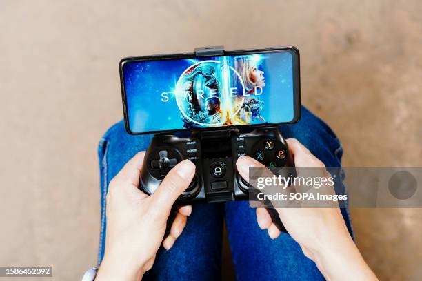 In this photo illustration, a person playing on a joystick and the Starfield logo displayed on a smartphone screen.