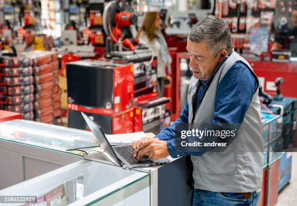business manager working at a hardware store and making a call while using a computer - bouwmarkt stockfoto's en -beelden
