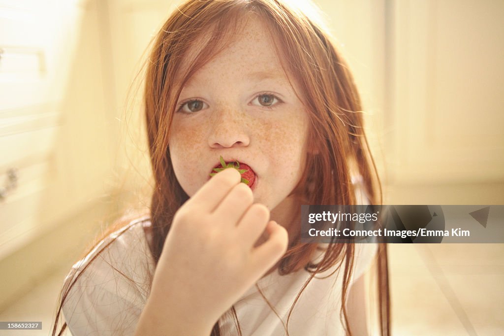 Girl eating strawberry on kitchen floor