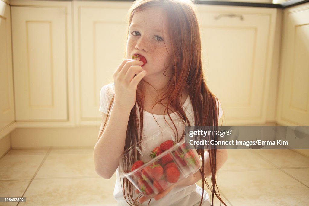 Girl eating strawberry on kitchen floor
