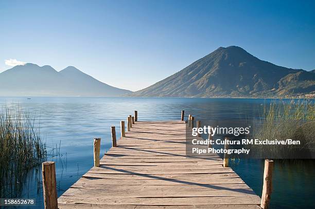 wooden pier stretching into still lake - lake atitlan - fotografias e filmes do acervo