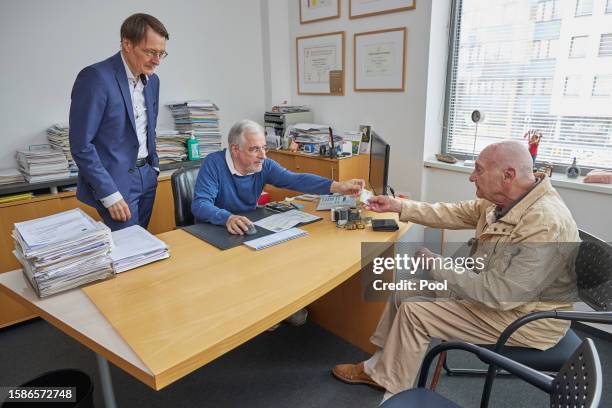 German Health Minister Karl Lauterbach observes as doctor Benny Levenson takes the health insurance card of 86-year-old Peter Jordan in order to be...
