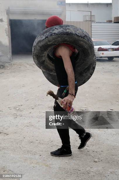 Bahraini Shiite Muslim carrying tyres, holds a molotov cocktail bomb, as protestors clashed with riot police on March 31 during a demonstration...