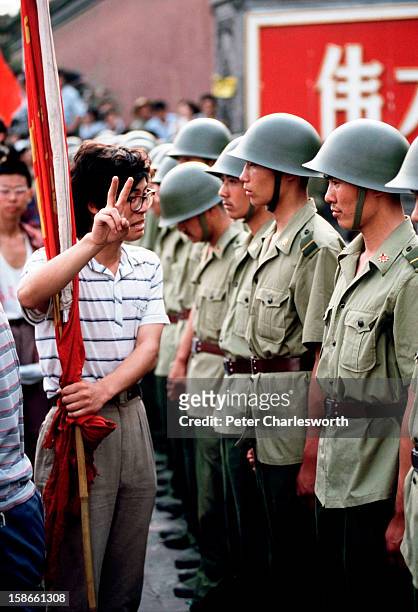 Pro-democracy demonstrator gives the V for Victory sign to soldiers who are lined up, standing guard outside the Chinese Communist Party's...