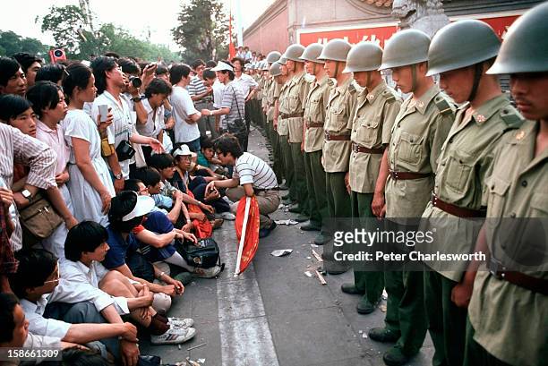 Pro-democracy demonstrators sit in front of soldiers who are lined up, standing guard outside the Chinese Communist Party's headquarters on Chiangan...