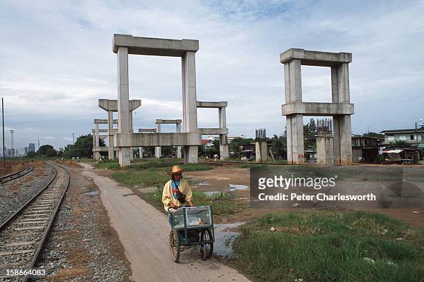 Street vendor walks past stonehenge or the hopeless project. This is how the Thai public now refer to the concrete structures that line the road to...
