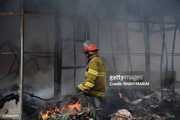 An Afghan firefighter walks past smouldering shopfronts after a huge fire swept through a market in Kabul on December 23, 2012. A huge fire swept...