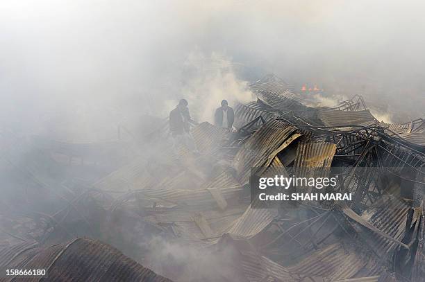 Afghan shopkeepers walk through the remains of smouldering shops after a huge fire swept through a market in Kabul on December 23, 2012. A huge fire...