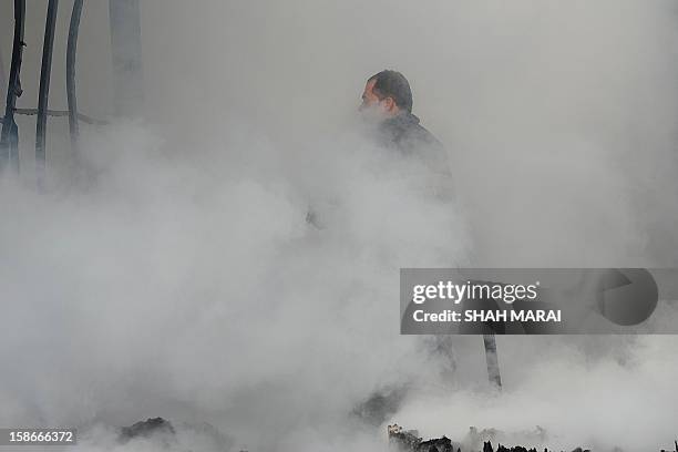 An Afghan firefighter walks past smoke and smouldering debris at the scene after a huge fire swept through a market in Kabul on December 23, 2012. A...