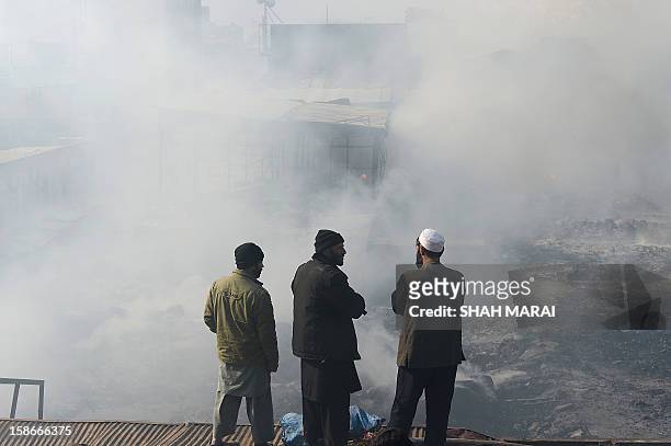Afghan shopkeepers look on as they stand over the smoldering remains of shops after a huge fire swept through a market in Kabul on December 23, 2012....