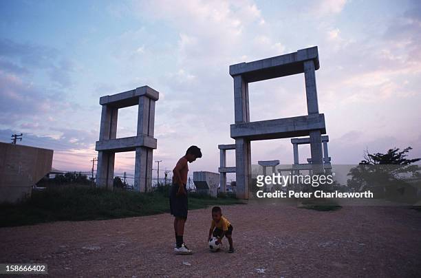 Economic collapse of 1997. A man plays football with a little boy in the shadow of the failed Hopewell overhead railway project. The Thai public now...