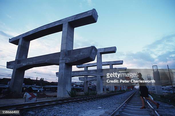 Economic collapse of 1997. A woman walks across railway tracks in the shadow of the failed Hopewell overhead railway project. The Thai public now...